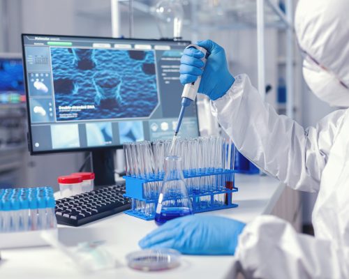 Virolog coducting experiment in the course of coronavirus pandemic with micropipette. Chemist in modern laboratory doing research using dispenser during global epidemic with covid-19.